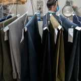 Giuseppe ci conduce poi nella parte retrostante colma di grucce con su poggiati pantaloni...